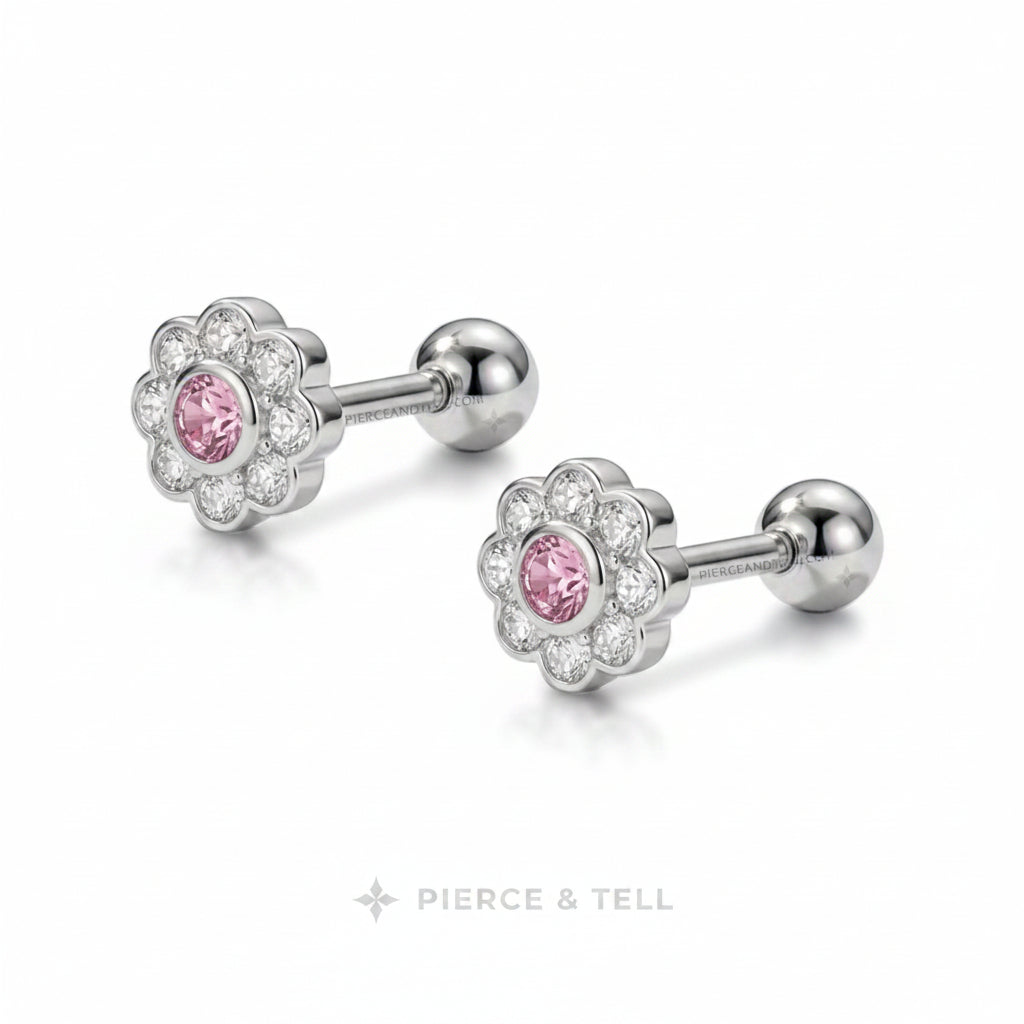 A pair of flower-shaped cartilage piercings by Pierce & Tell, featuring a silver-toned metal halo with a central pink gemstone and clear accent stones, shown on a white background.