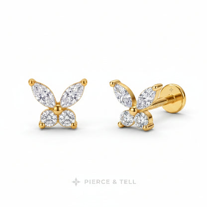 A pair of gold butterfly stud earrings with marquise and round-cut clear gemstones, shown on a white background with the PIERCE & TELL logo below.