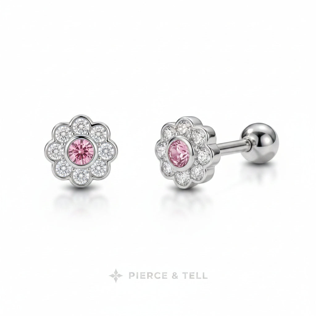 A pair of flower-shaped stud earrings with a silver-toned metal setting, featuring a central round pink gemstone surrounded by a halo of small clear stones. One earring is shown facing forward and the other is angled to show the post and ball back.