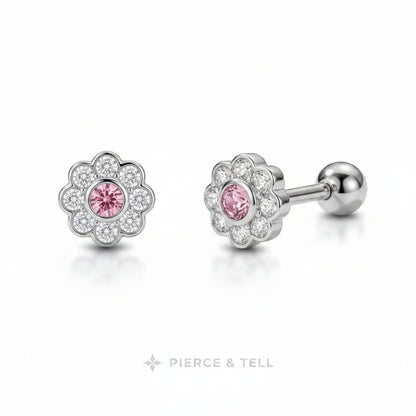 A pair of flower-shaped stud earrings with a silver-toned metal setting, featuring a central round pink gemstone surrounded by a halo of small clear stones. One earring is shown facing forward and the other is angled to show the post and ball back.