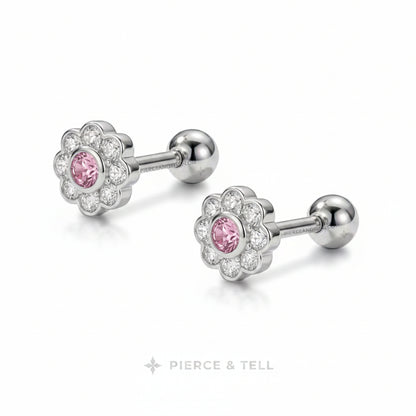 A pair of flower-shaped cartilage piercings by Pierce & Tell, featuring a silver-toned metal halo with a central pink gemstone and clear accent stones, shown on a white background.