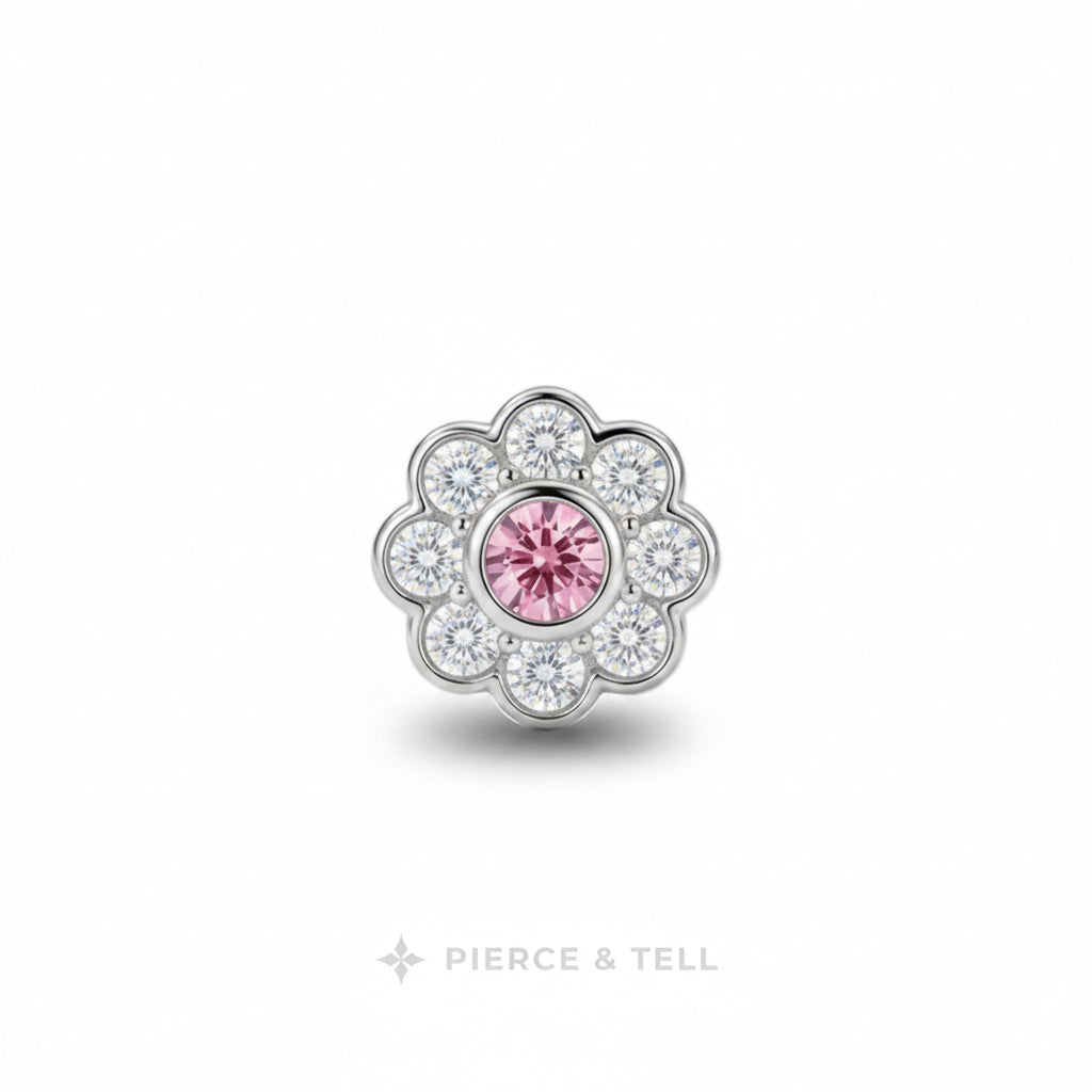A flower-shaped silver-toned jewelry charm featuring a central round pink gemstone surrounded by a halo of clear cubic zirconia stones, shown on a white background with the PIERCE & TELL logo below.