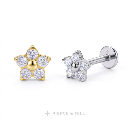 Two flower-shaped stud earrings on a white background, one in yellow gold and one in silver. Each earring has five clear gemstones, with the center of the gold earring filled with a gold bead and the center of the silver earring filled with a silver bead.