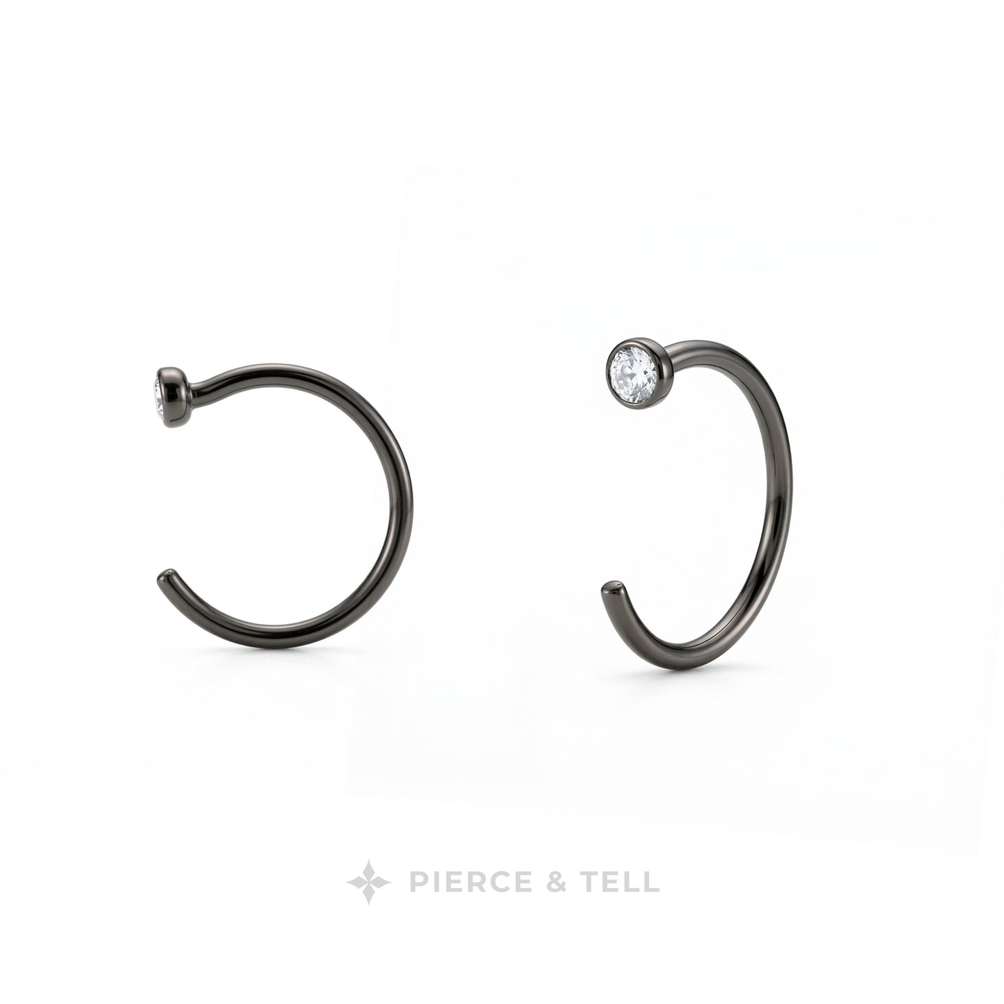 Two dark metallic C-shaped hoop earrings on a white background, one plain and one with a small clear gemstone, with the brand name 'PIERCE & TELL' at the bottom.