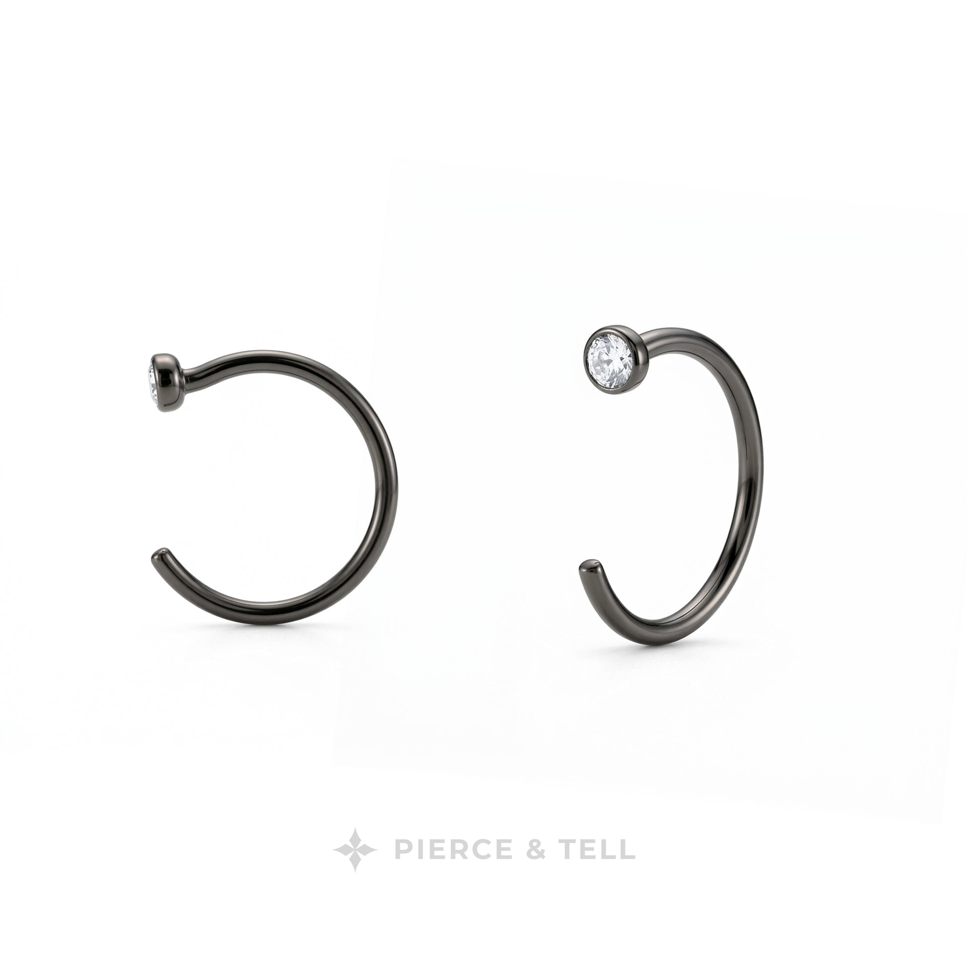 Two dark metallic C-shaped hoop earrings on a white background, one plain and one with a small clear gemstone, with the brand name 'PIERCE & TELL' at the bottom.