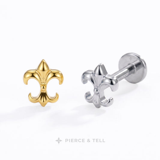 Two fleur-de-lis body jewelry studs by Pierce & Tell, one in polished yellow gold and the other in polished silver, displayed on a clean white background.