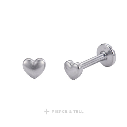 Silver heart-shaped labret stud earrings shown from front and side angles on a white background, with the PIERCE & TELL logo at the bottom.