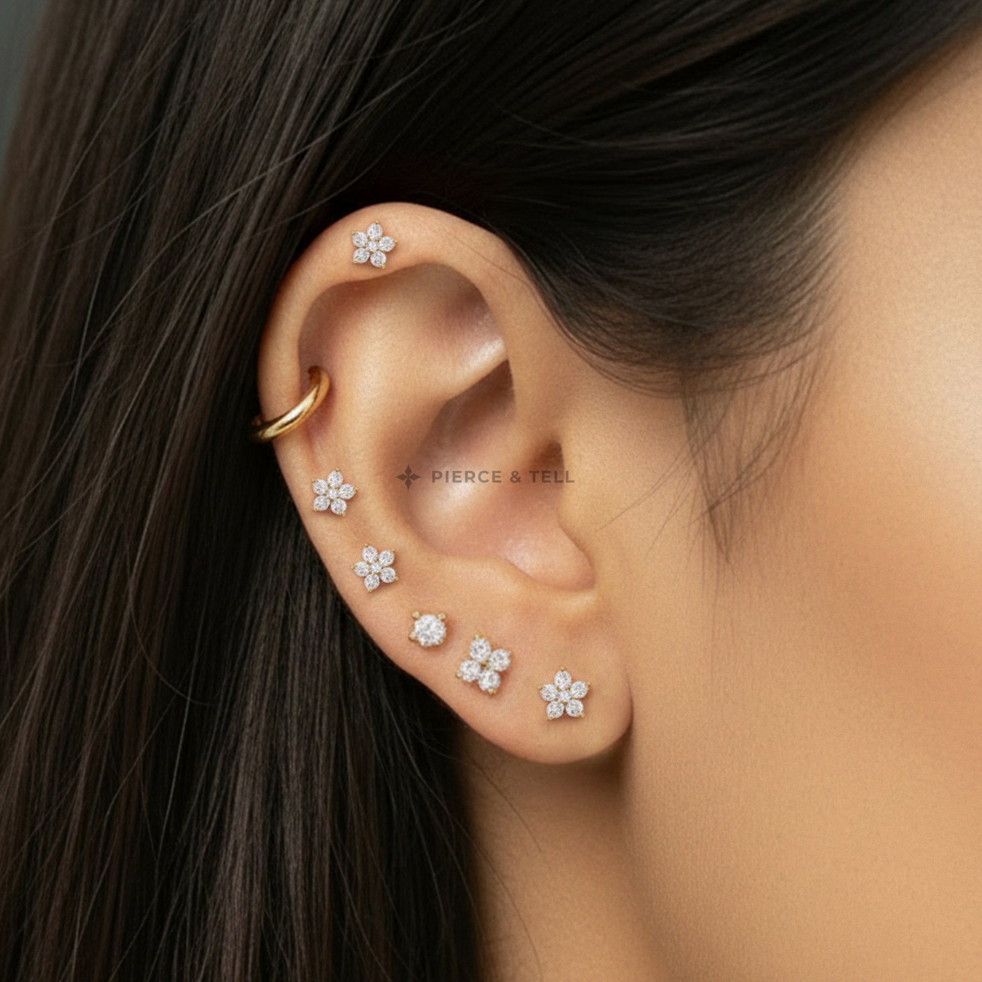 Close-up of an ear with floral earrings and a gold earring, branded 'Pierce & Tell'.