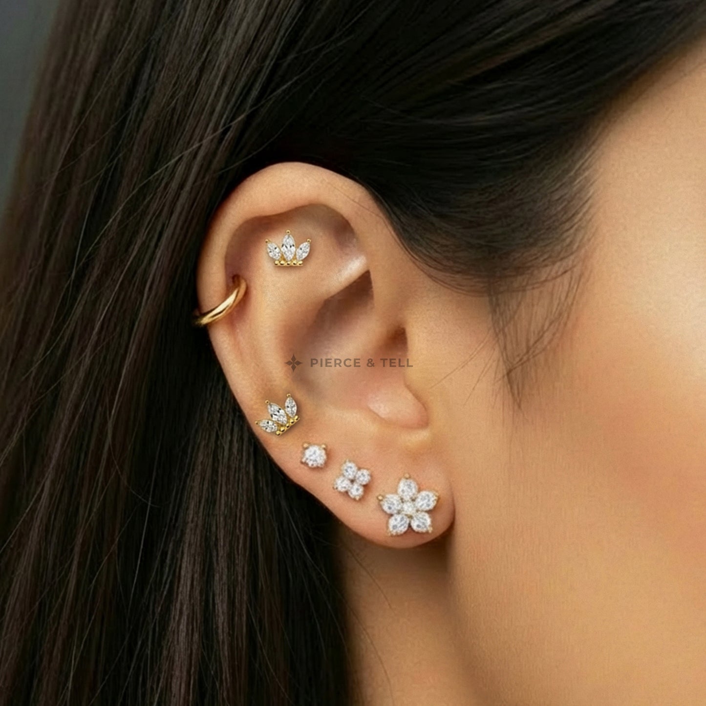 Close-up of an ear wearing gold and diamond earrings with a neutral background.