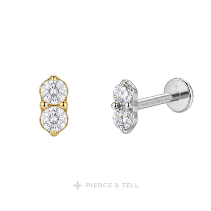 Two small stud earrings on a white background: one in yellow gold and one in silver, each featuring two round clear gemstones. The silver earring is shown from the side with a post and flat back.