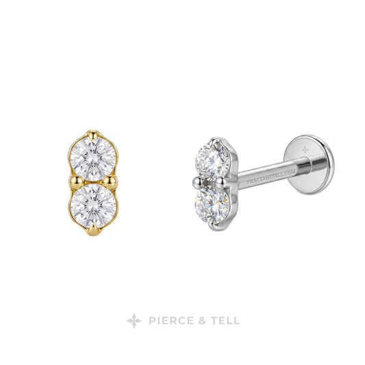 Two small stud earrings on a white background: one in yellow gold and one in silver, each featuring two round clear gemstones. The silver earring is shown from the side with a post and flat back.