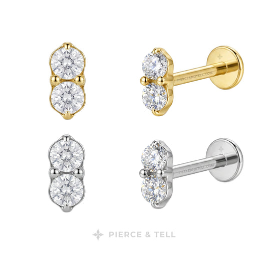 Four stud earrings shown on a white background, each in a different metal finish: yellow gold, white gold, silver, and platinum. Each earring features two round clear gemstones in a prong setting.
